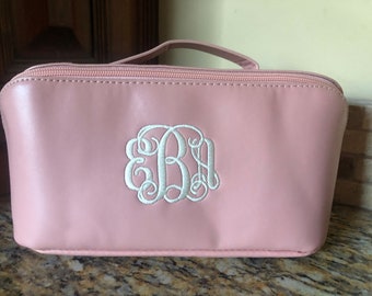 May include: A pale pink zippered travel bag with a white embroidered monogram "EBA" on the front.