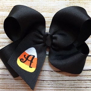 May include: Black hair bow with a candy corn design and the letter "A" embroidered in the center.