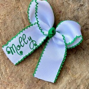 May include: White ribbon bow with green trim and the name "Molly" embroidered in green with shamrock accents.