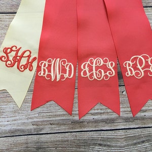 May include: Four fabric ribbon banners with embroidered monograms. The banners are in shades of red and cream. The monograms are "SAH", "BWD", "ECS", and "RPJ".
