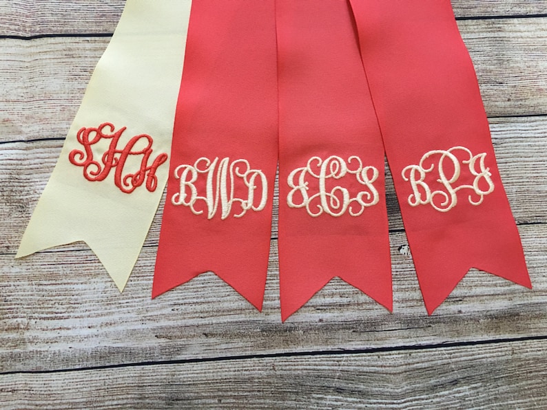 May include: Four fabric ribbon banners with embroidered monograms. The banners are in shades of red and cream. The monograms are "SAH", "BWD", "ECS", and "RPJ".