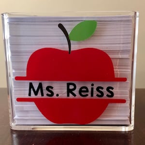 May include: A clear acrylic desk organizer with a red apple design and the text "Ms. Reiss" on the front.
