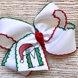 May include: White Christmas bow with green and red trim. The bow has an embroidered image of a green letter M with a Santa hat on top.