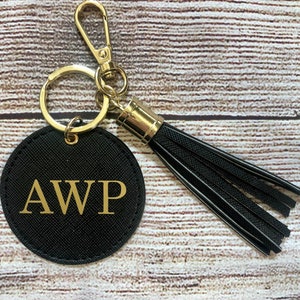 May include: Black round keychain with a gold metal ring and a gold metal clasp. The keychain has a black tassel and a black circle with the letters AWP in gold.