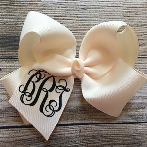 May include: A large ivory bow with a black monogram of the letters "B.P." in a script font.