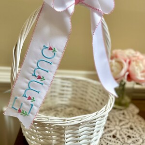 Puede incluir: Cesta blanca tejida con un gran lazo de cinta blanca y una cinta personalizada. La cinta est&aacute; bordada con el nombre "Emma" en letras azul claro con detalles florales rosas. Ideal para Pascua o para regalar.