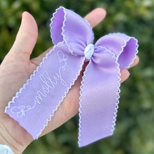 May include: A lavender bow with white scalloped edges and the name "Molly" embroidered in white thread.