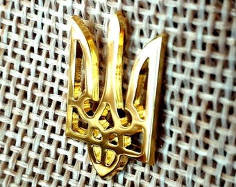 Może przedstawiać: Złoty metalowy trójząb, symbol narodowy Ukrainy, jest wyświetlany na tle tkanego płótna jutowego.