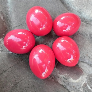 May include: Five shiny, bright red Easter eggs arranged in a star shape on a grey concrete surface.