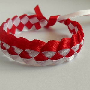 May include: A red and white braided bracelet made from ribbon. The bracelet is woven in a checkered pattern.