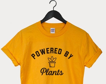 Puede incluir: Camiseta amarilla con texto negro que dice "Powered by Plants" y un pequeño icono de planta.