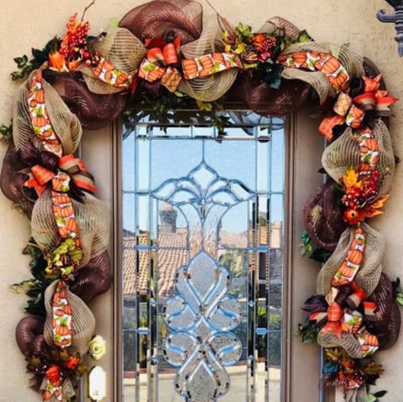 May include: A brown and beige mesh door wreath with fall-themed ribbon and accents. The wreath is decorated with pumpkins, leaves, and berries.