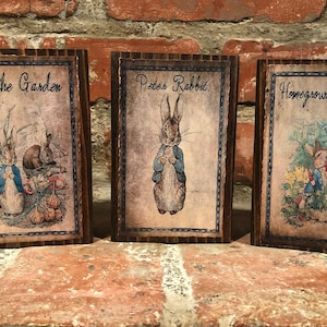 May include: Three framed vintage-style prints featuring illustrations of Peter Rabbit. The prints are in dark wooden frames and depict scenes from the classic children's story, including text that reads "In the Garden", "Peter Rabbit", and "Homegrown Carrots".