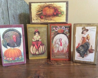 May include: A collection of five rectangular wooden blocks with vintage Thanksgiving-themed illustrations. The images feature turkeys, pumpkins, and children, with text such as "Thanksgiving Greeting" and "Best Wishes for a Happy Thanksgiving."
