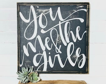 May include: Black wooden sign with white calligraphy that reads "You me & the girls".