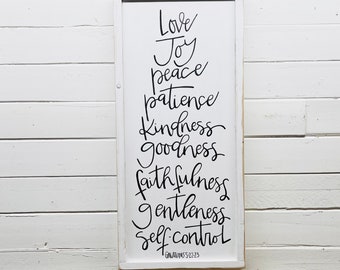 May include: White wooden sign with black calligraphy listing the fruits of the spirit: love, joy, peace, patience, kindness, goodness, faithfulness, gentleness, and self-control. The text "Galatians 5:22-23" is included at the bottom of the sign.