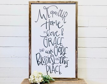 May include: A wooden sign with the text "We open our home in love & grace and ask God's blessing on this place" written in black calligraphy.