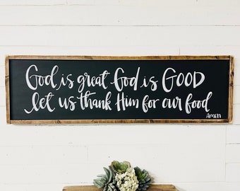 May include: A black framed sign with white calligraphy that reads "God is great God is GOOD let us thank Him for our food Amen".