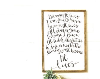 May include: A framed wood sign with a white background and black calligraphy. The text reads "Because He lives I can face tomorrow because He lives All fear is gone because I know He holds the future & life is worth the living just because He lives".