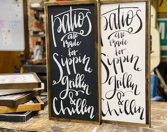 May include: Two wooden signs with the text "Patios are made for sippin' grillin' & chillin'" in black script on a white background and white script on a black background.
