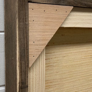 May include: Close-up of a wooden frame with a light brown wood triangle inset. The frame is made of dark brown wood with a distressed finish.