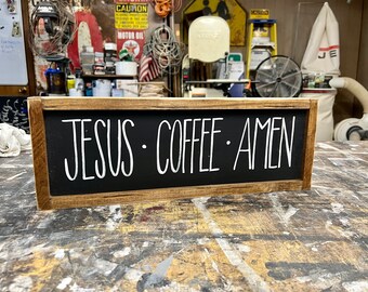 May include: A wooden sign with a black background and white lettering that reads "JESUS COFFEE AMEN".