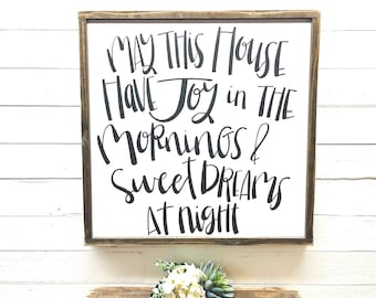 May include: A white wooden sign with black calligraphy that reads "May this house have joy in the mornings & sweet dreams at night".