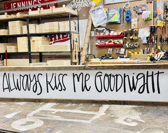 May include: A wooden sign with a white background and black lettering that reads "Always Kiss Me Goodnight".