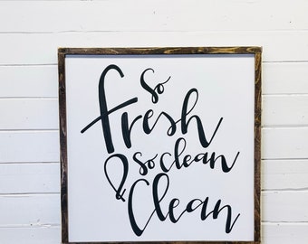 May include: A white wooden sign with a brown frame, featuring black calligraphy that reads "so fresh & so clean clean".