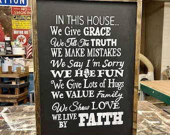 May include: A black framed sign with white text that reads "In this house... We give grace, We tell the truth, We make mistakes, We say I'm sorry, We have fun, We give lots of hugs, We value family, We show love, We live by faith."