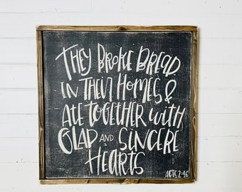 May include: Black wooden sign with white text that reads "They broke bread in they homes & ate together with glad and sincere hearts Acts 2:46".