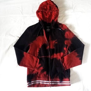Puede incluir: Sudadera con capucha roja y negra con estampado tie-dye y rayas blancas en el dobladillo inferior.