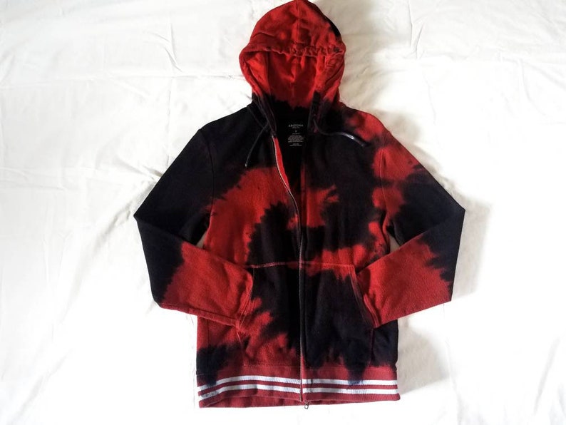 Puede incluir: Sudadera con capucha roja y negra con estampado tie-dye y rayas blancas en el dobladillo inferior.