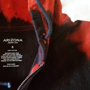 Puede incluir: Una sudadera con capucha de color negro y rojo con efecto tie-dye y cierre de cremallera. La etiqueta dice "Arizona Jean Co" y "S" para el tama&ntilde;o. Las instrucciones de cuidado incluyen lavar a m&aacute;quina con agua fr&iacute;a, ciclo delicado, usar solo blanqueador sin cloro si es necesario, secar en secadora a baja temperatura, planchar a temperatura media si es necesario, no planchar sobre la impresi&oacute;n. Hecho en India. Proveedor 76441-5RNP93677.