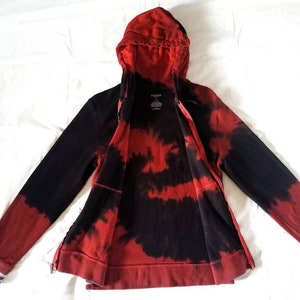 Puede incluir: Sudadera con capucha de color rojo y negro tie-dye con cierre de cremallera y capucha. La sudadera tiene ribetes blancos en las mangas y una peque&ntilde;a etiqueta en la parte delantera que dice "Arden B."