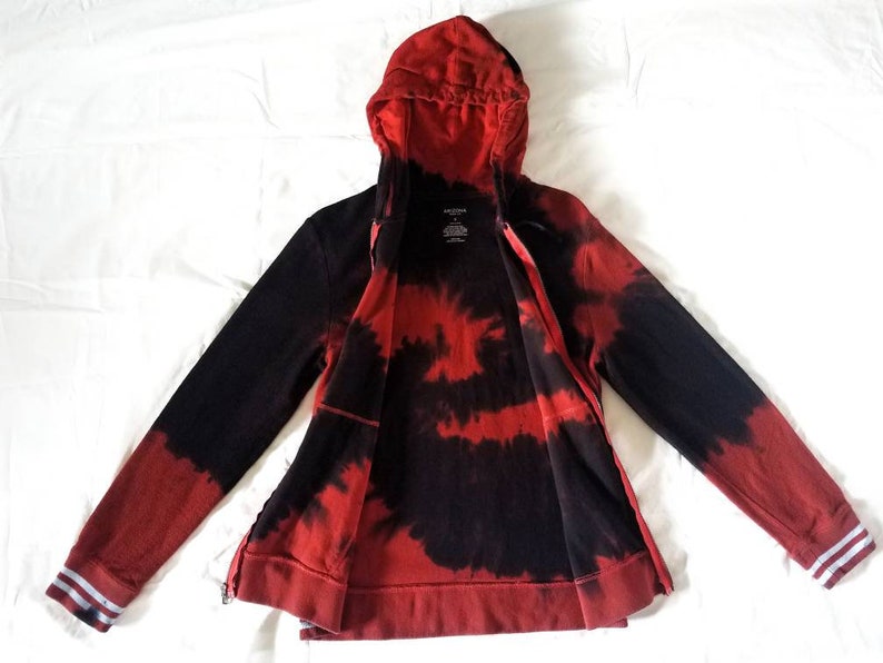 Puede incluir: Sudadera con capucha de color rojo y negro tie-dye con cierre de cremallera y capucha. La sudadera tiene ribetes blancos en las mangas y una peque&ntilde;a etiqueta en la parte delantera que dice "Arden B."