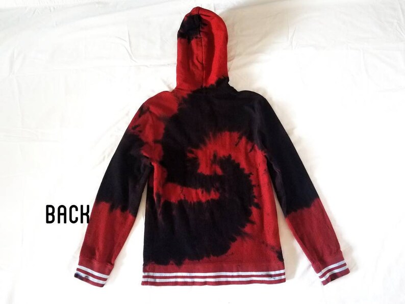 Puede incluir: Sudadera con capucha de color rojo y negro tie-dye con rayas blancas en los pu&ntilde;os y la cintura. La sudadera tiene una capucha con cord&oacute;n.