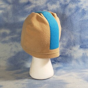 May include: A tan fleece beanie with a blue stripe down the side. The beanie is on a white mannequin head.