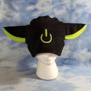 May include: Black fleece hat with green trim and a power button symbol on the front. The hat has two large, floppy ears.