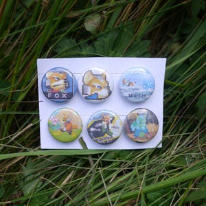 May include: A collection of six colorful pinback buttons featuring various images of a fox character. The buttons have different designs, including pixel art and illustrations, with text such as "FOX" and "nice shorten". The buttons are displayed on a white card.