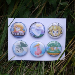 May include: Six round blue and white buttons with different images. The buttons feature a princess character, a character with a crown, a character with a crown and a flower, a character with a crown and a flower, a character with a crown and a flower, and a character with a crown and a flower.