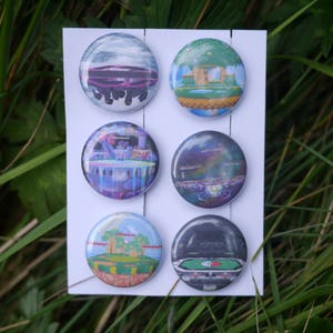 May include: Six round buttons with different images printed on them. The buttons are arranged in two rows of three. The images are of a purple and blue castle, a green island with a tree, a purple and blue sky with stars, a green island with a tree, a purple and blue sky with stars, and a green island with a tree.