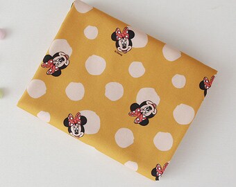 Puede incluir: Tela amarilla con estampado de lunares blancos y una imagen repetida de Minnie Mouse. La tela tiene el texto "©Disney" impreso.