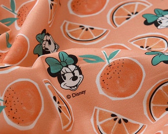 Puede incluir: Tela de color melocotón con un patrón repetido de rodajas de naranja e imágenes de dibujos animados de Minnie Mouse. La tela tiene el texto "© Disney" impreso.