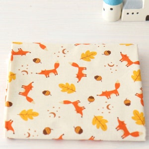 May include: White fabric with a repeating pattern of orange foxes, yellow leaves, and brown acorns. The fabric has a subtle texture.