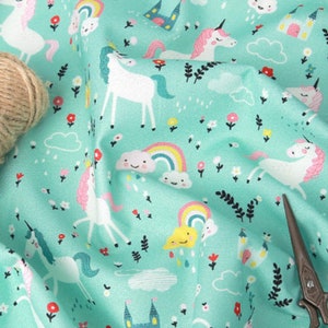 May include: A turquoise fabric with a repeating pattern of white unicorns, rainbows, clouds, and flowers. The fabric is ideal for crafting projects such as clothing, accessories, and home decor.