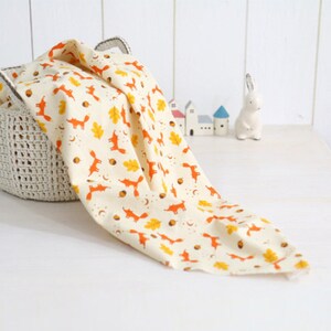 May include: A cream-colored fabric with a repeating pattern of orange foxes, yellow leaves, and brown acorns. The fabric is draped over a crocheted basket.
