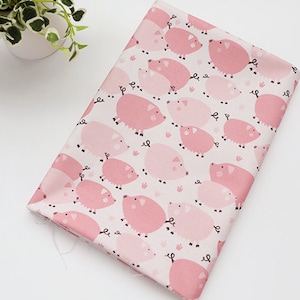 May include: Pink fabric with a repeating pattern of pink pigs. The pigs are different sizes and shades of pink.