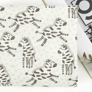 Könnte beinhalten: Weißer Stoff mit einem sich wiederholenden Muster aus schwarz-weißen Zebra-Illustrationen. Die Zebras sind in verschiedenen Posen, einige stehen, einige rennen und einige schauen zur Seite. Der Stoff hat eine subtile Textur.