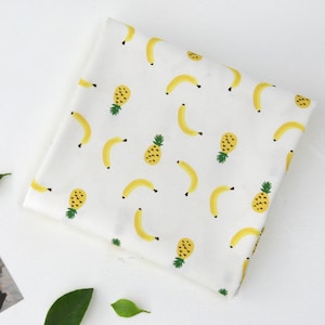 Peut inclure: Tissu blanc avec un motif répété de bananes jaunes et d'ananas. Le tissu est parfait pour des projets de bricolage comme le quilting, la couture et la fabrication d'accessoires.